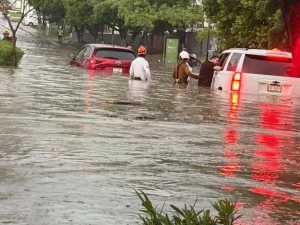 Vehículos varados en una calle inundada de Tuxtla Gutiérrez mientras rescatistas auxilian a ocupantes