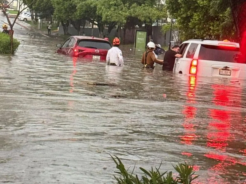 Vehículos varados en una calle inundada de Tuxtla Gutiérrez mientras rescatistas auxilian a ocupantes